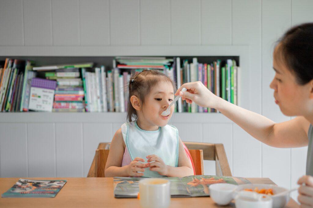 A mother feeds a spoonful of carrots to her toddler.