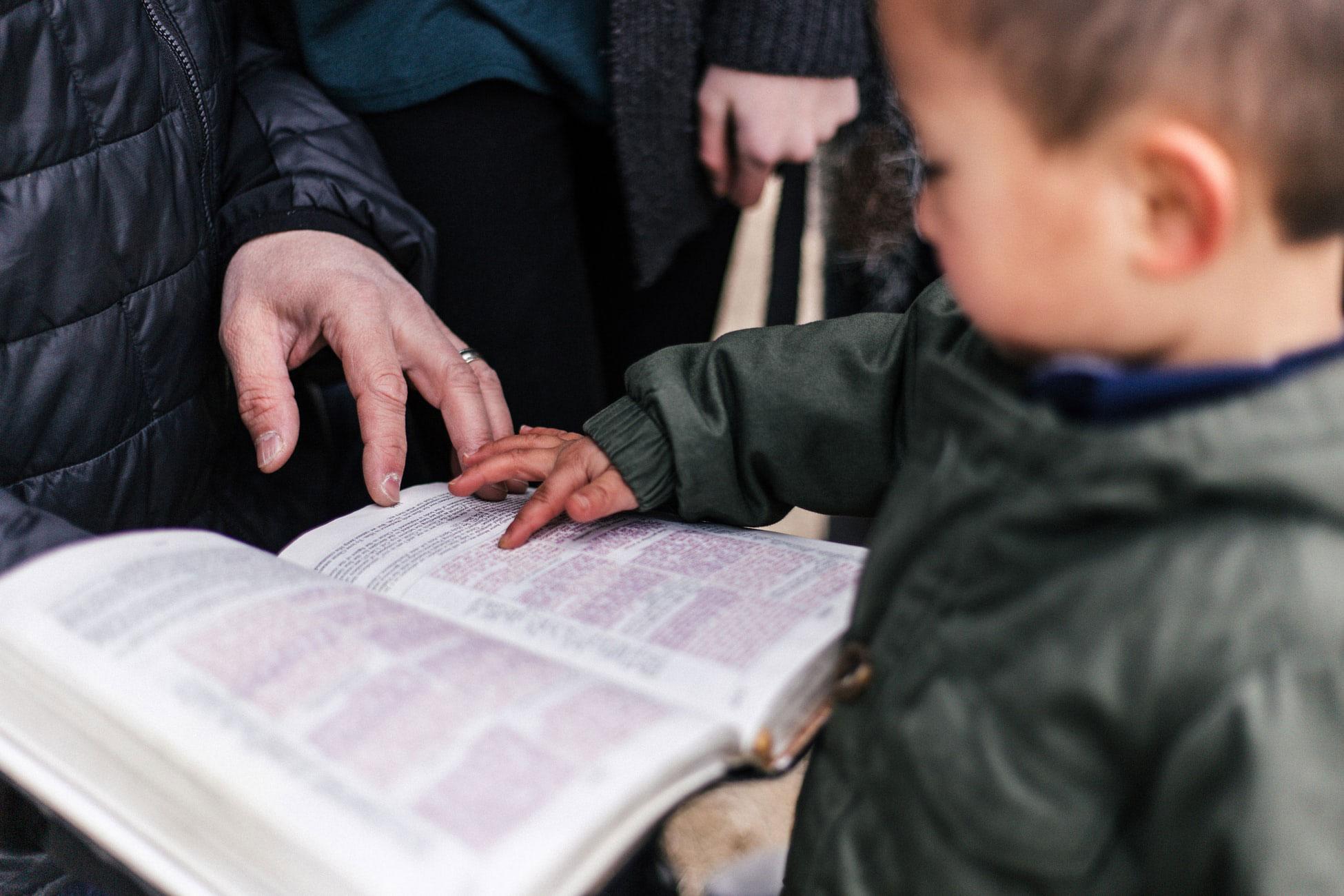 A toddler points at passages in a Bible held by an adult.